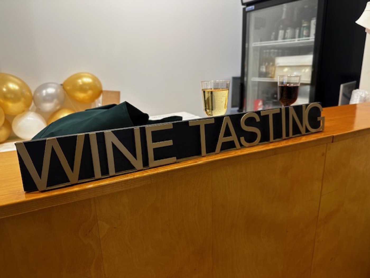 Wine tasting sign on a wooden bar with two pours and balloon décor.