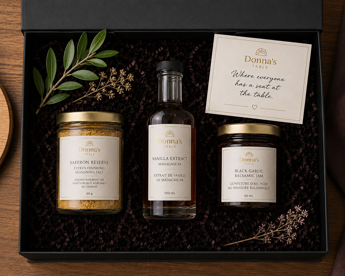 Donna's Table gift box with Saffron Reserve, Vanilla Extract, and Black Garlic Balsamic Jam nestled in dark crinkle paper with a brand card.